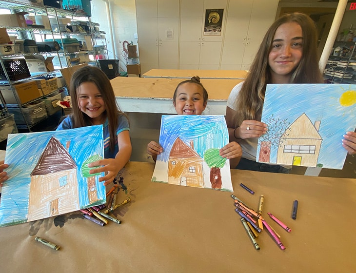 3 Kids holding up drawings of houses