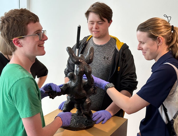 Three visually impaired people touching a sculpture while wearing nitrile gloves