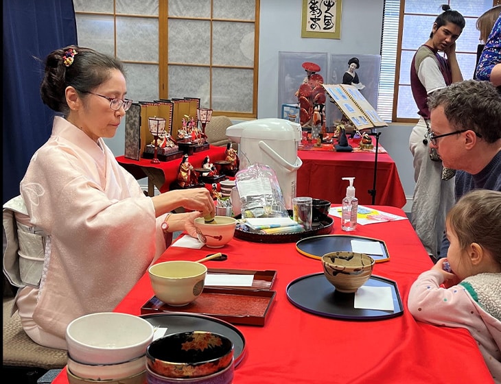 Traditional Japanese tea ceremony where two people sit across a table from on another and are served tea.
