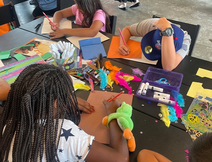 Children sitting at a table working on creating colorful artworks.