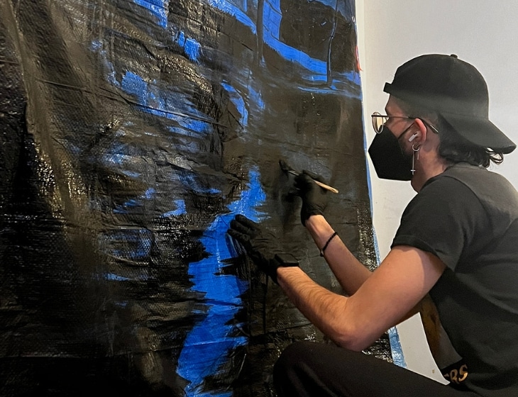 Artist Lionel Cruet using black paint on a blue FEMA tarp. Photo by Lionel Cruet Studio.