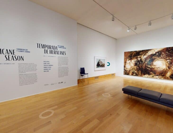 View of the first gallery space in the virtual tour of "Hurricane Season," showing the wall vinyl text introducing the exhibition, a painting by Hew Locke, and a large ceramic mural by Teresita Fernández.
