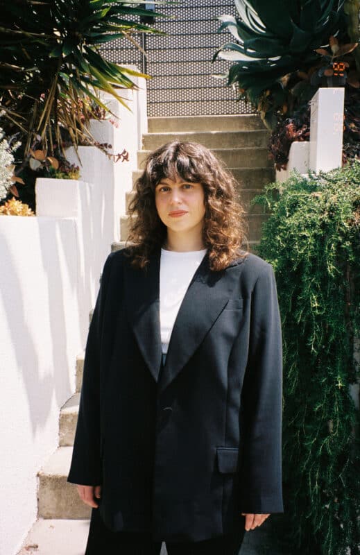 Ashton Cooper portrait photo - woman wearing black suit standing outside in front of green foliage and staircase