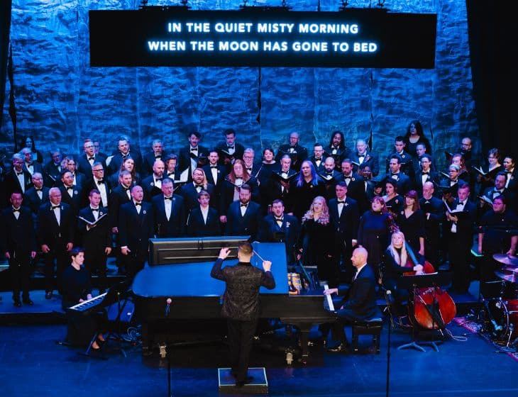 Des Moines Gay Men's Chorus concert. Large group of people wearing black suits, standing and singing.