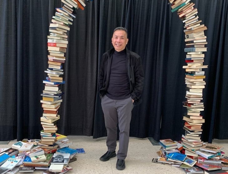 Vinh Nguyen standing under an archway made from books