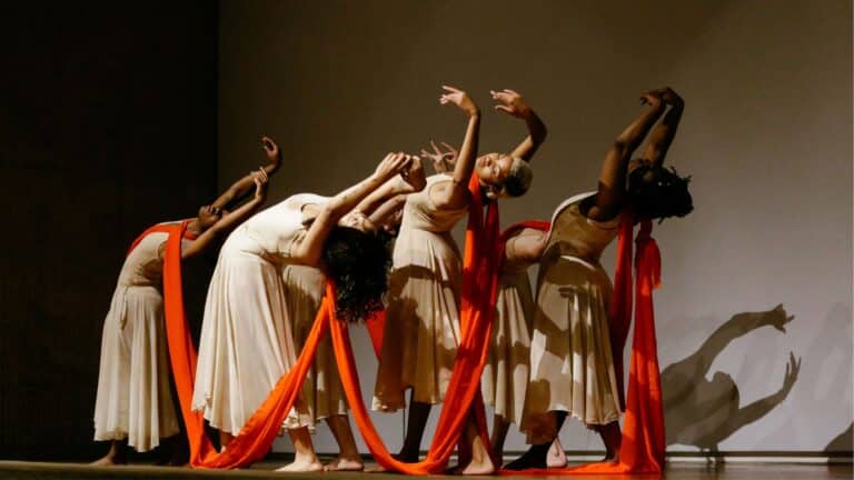 THREADS Dance Performance at the Des Moines Art Center - six dancers on stage in tan dance uniforms and an orange thread running between them.