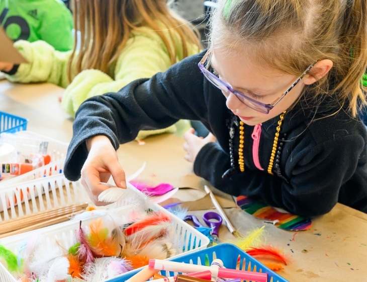 Girl in the Art Center studios making an artwork, picking out colored feathers from a box.